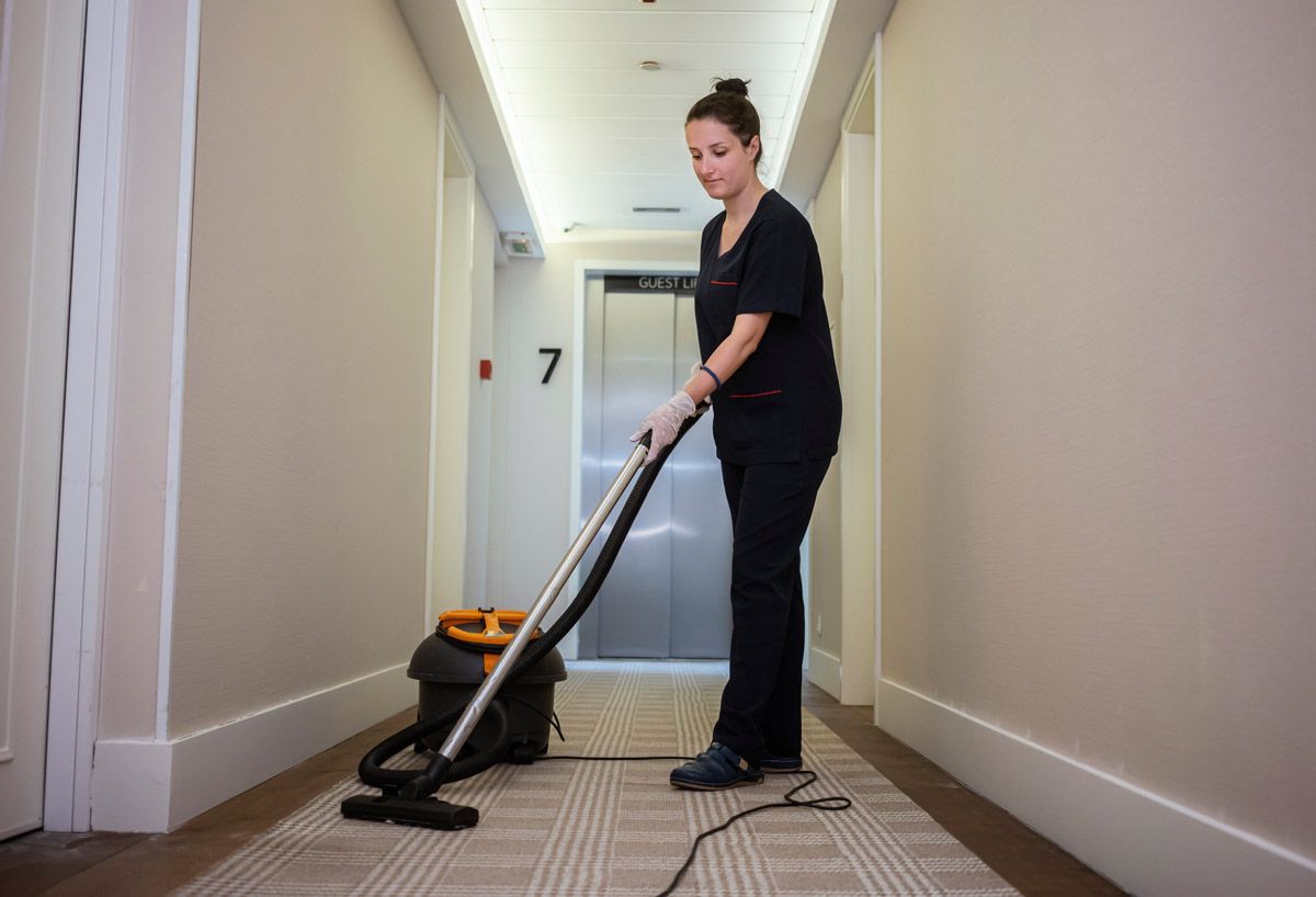 A woman is using a vacuum cleaner to clean a hallway.