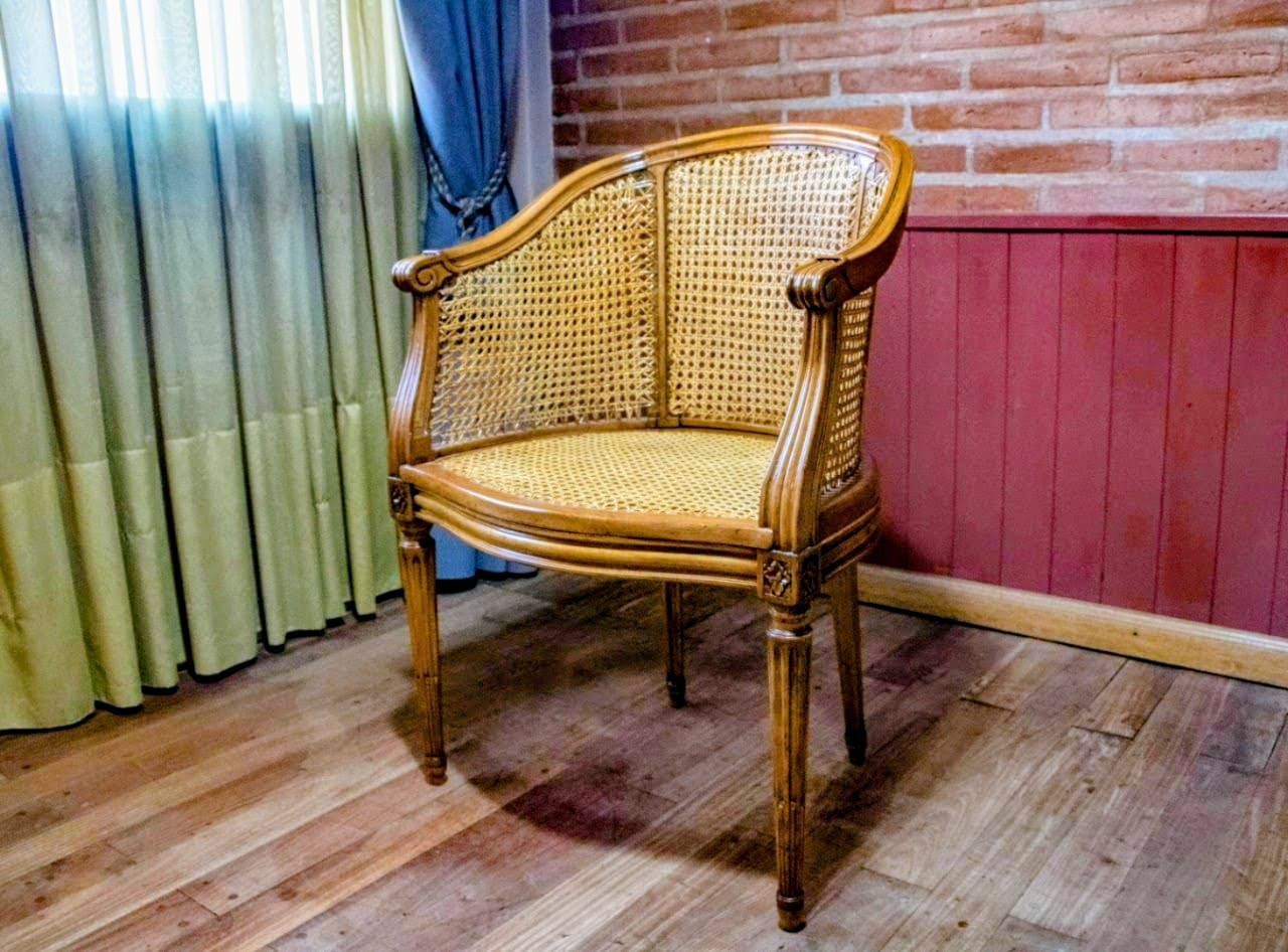Silla de mimbre sobre suelo de madera frente a una pared de ladrillo y paneles rojos con una cortina verde.