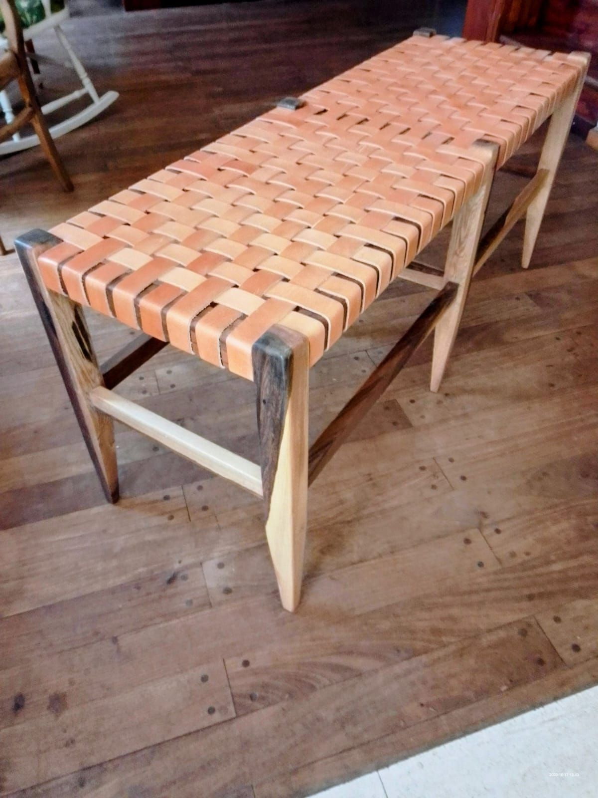 Banco con asiento tejido en cuero y estructura de madera clara, sobre suelo de madera.