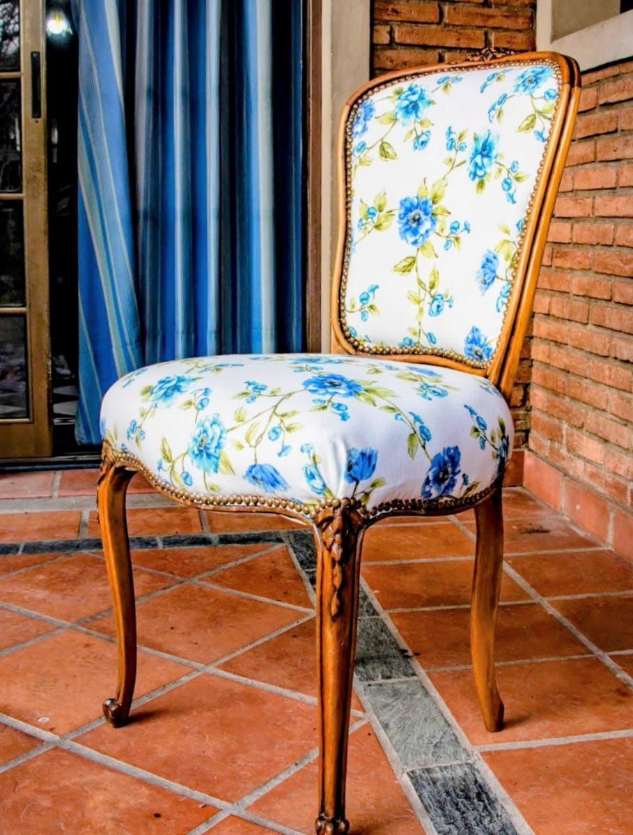 Una silla vintage con tela blanca, estampado floral azul, estructura de madera y baldosas de terracota.