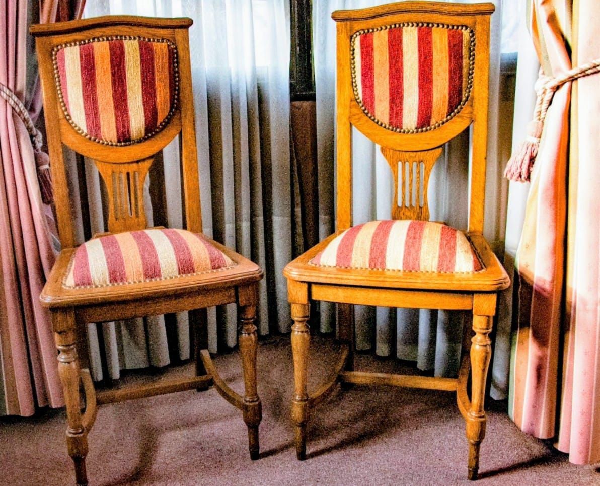 Dos sillas de madera con cojines y respaldos de rayas naranjas y blancas delante de cortinas.