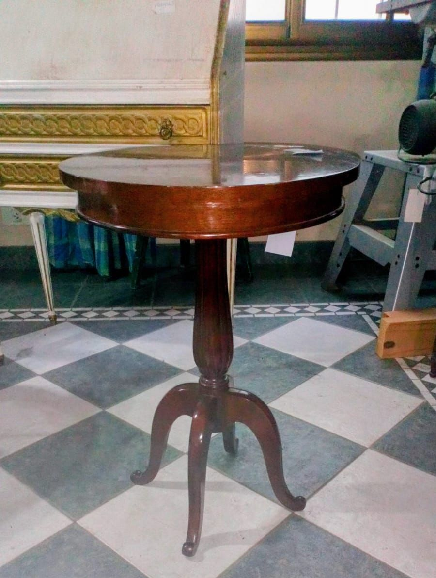 Mesa auxiliar redonda de madera de color marrón con tres patas curvas sobre suelo cuadriculado.
