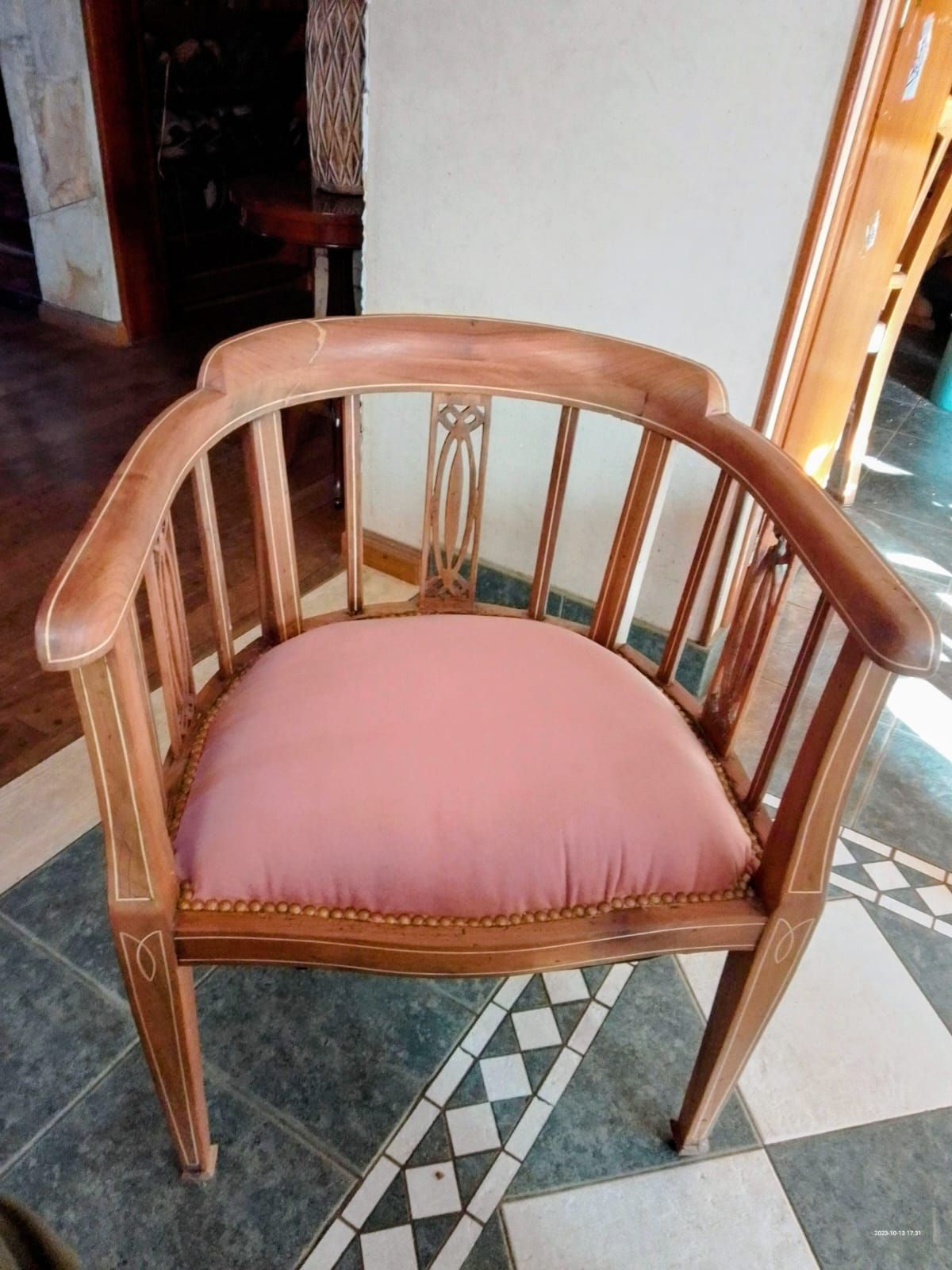 Sillón de madera con cojín rosa, sobre suelo de baldosas.