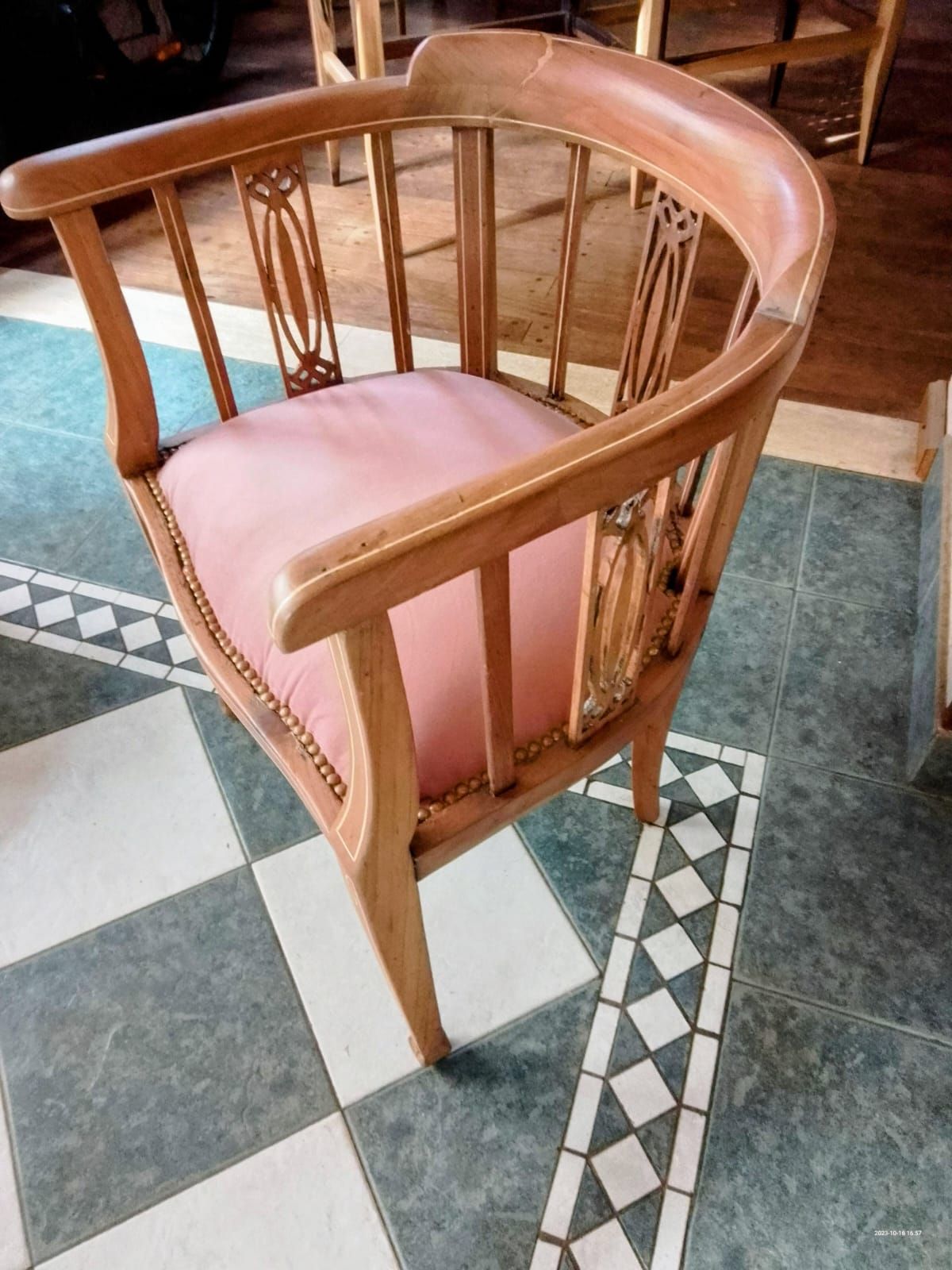 Sillón de madera con cojín rosa, sobre suelo de baldosas.