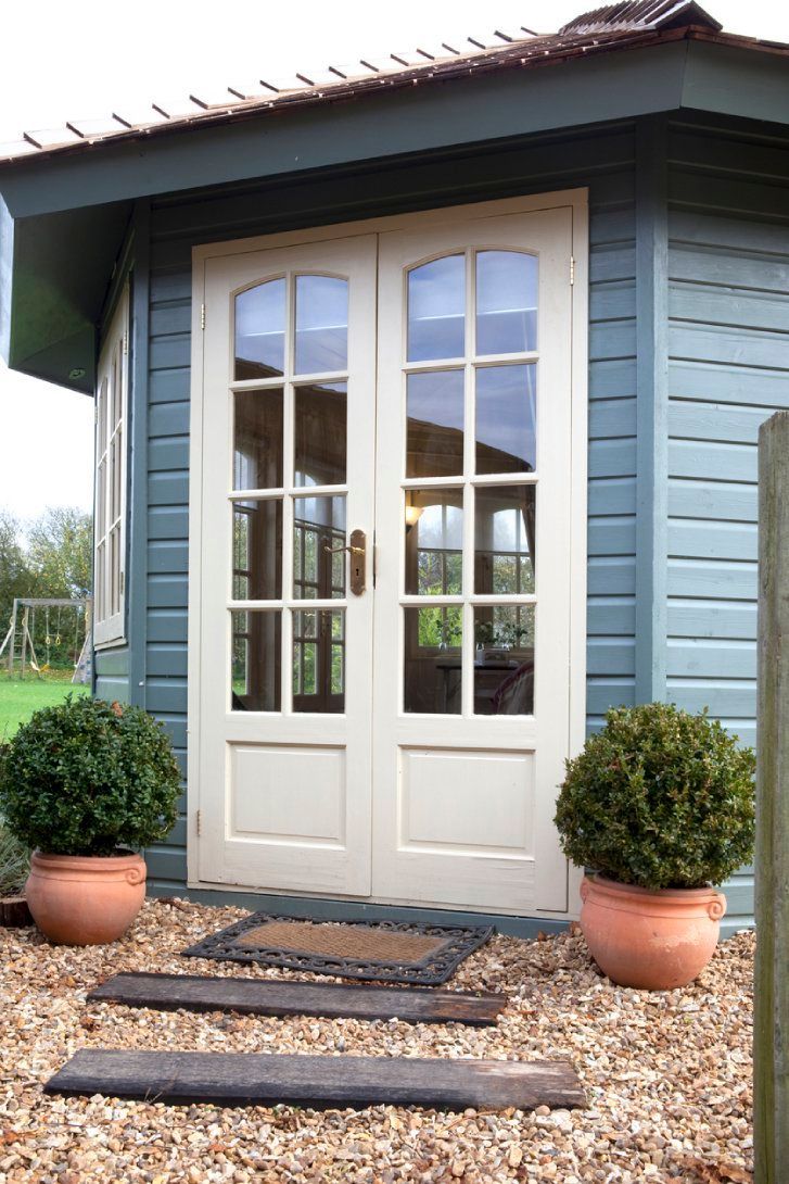 A blue house with white doors and potted plants in front of it