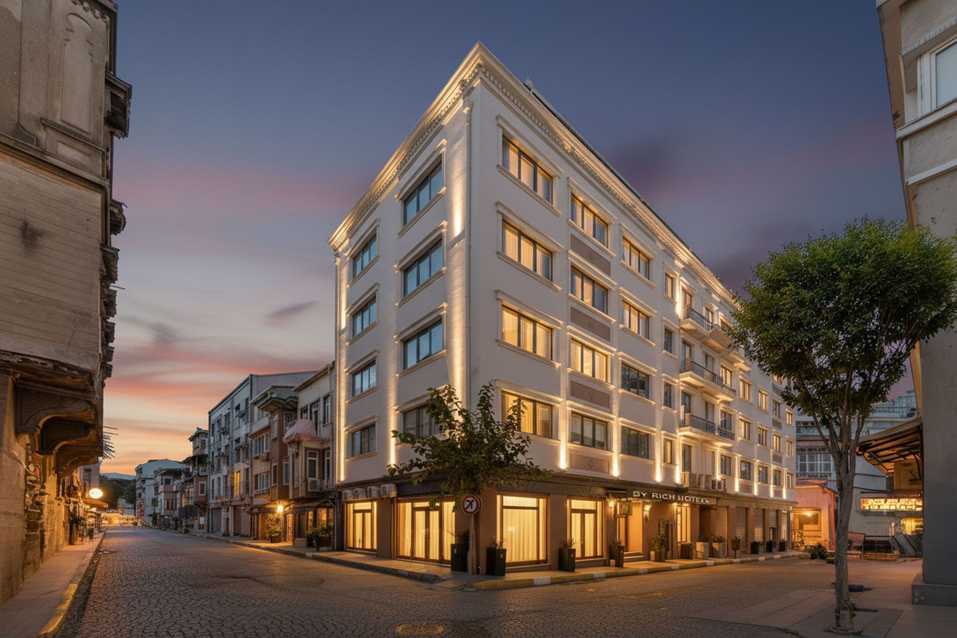 Istanbul By Rich Hotel | Hotel building on a cobblestone street corner at dusk, illuminated lights, and a colorful sky.