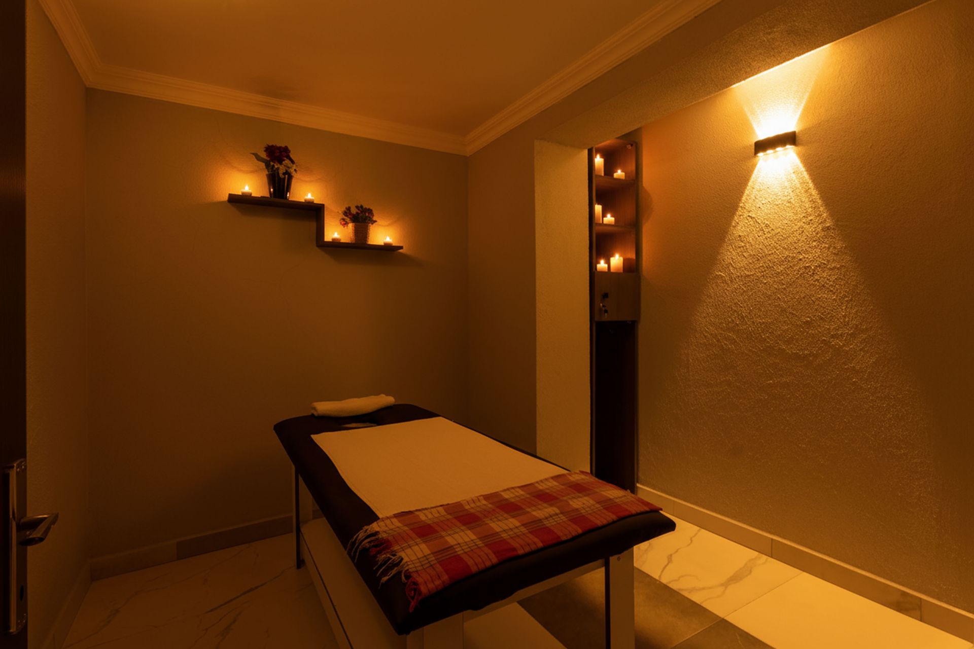 Mays Otel | Massage room with massage table, candles on shelves, and wall sconces, creating a relaxing ambiance.