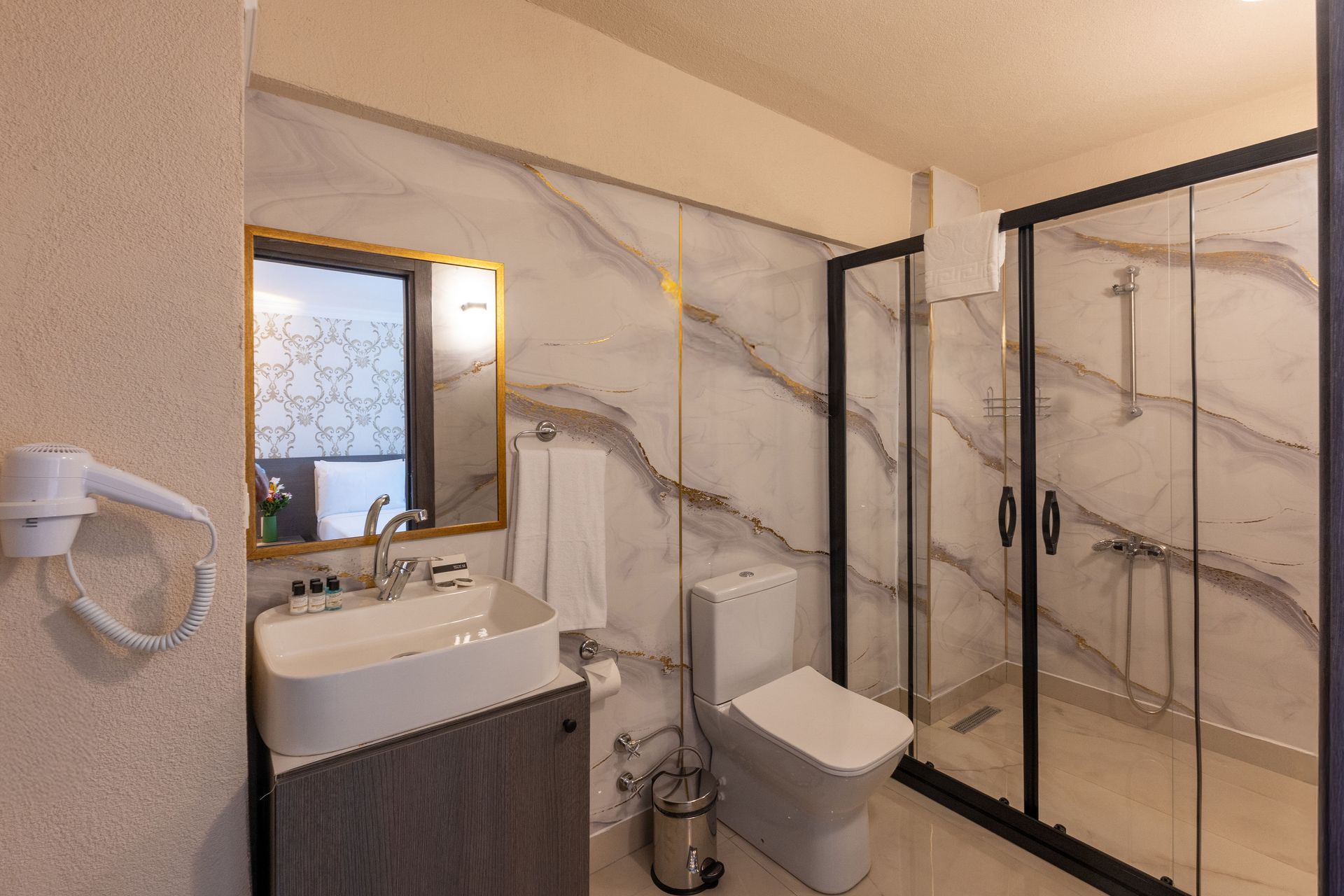 Istanbul By Rich Hotel | Bathroom with marble-effect wall, glass shower, toilet, sink with mirror, and hairdryer.