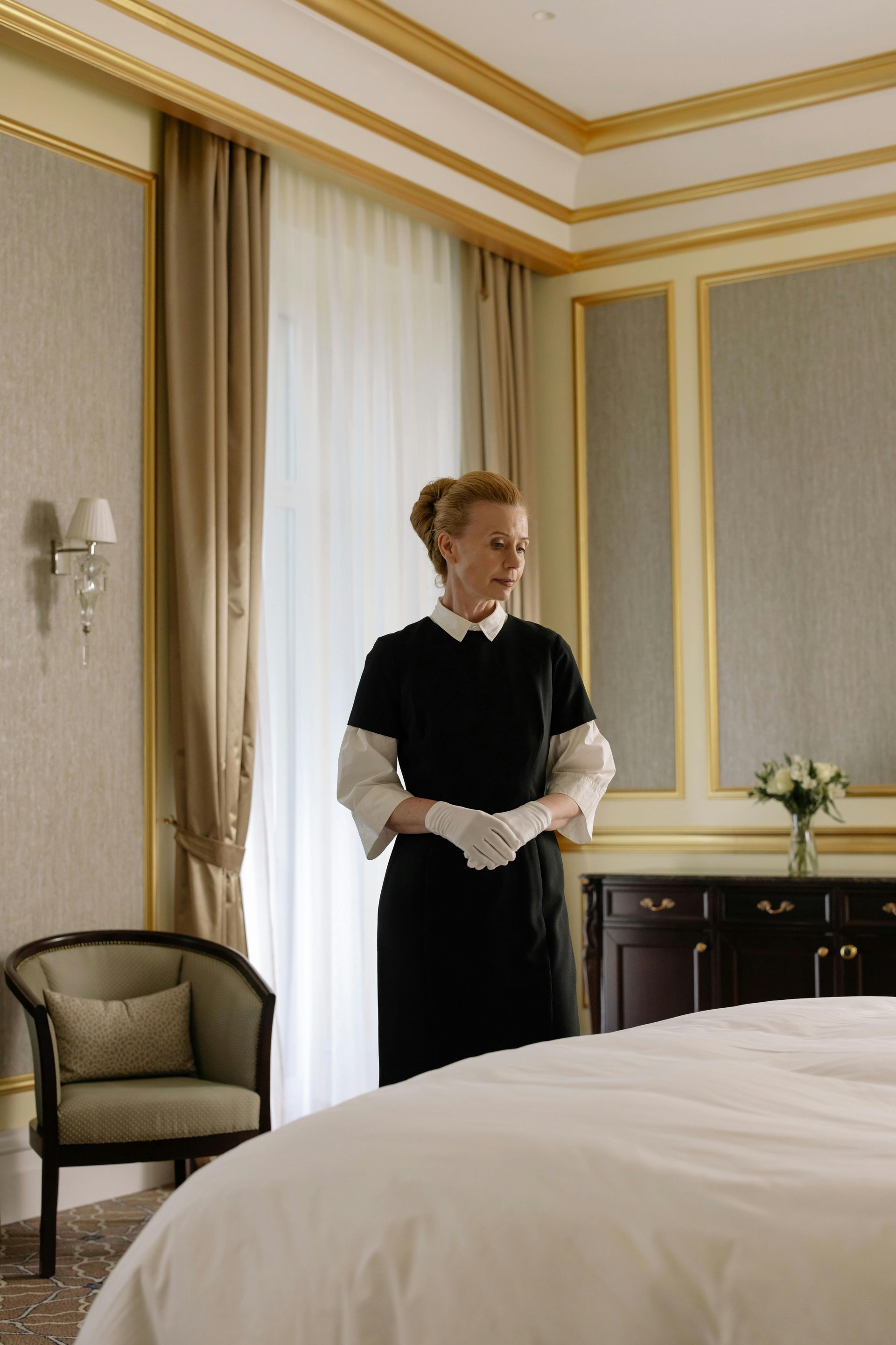 Mays Otel | In a hotel room, a housekeeping stands beside the prepared bed.