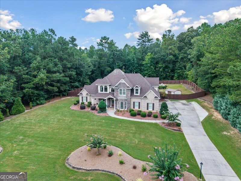 Large two-story house with green lawn, driveway, and surrounding trees under a blue sky.