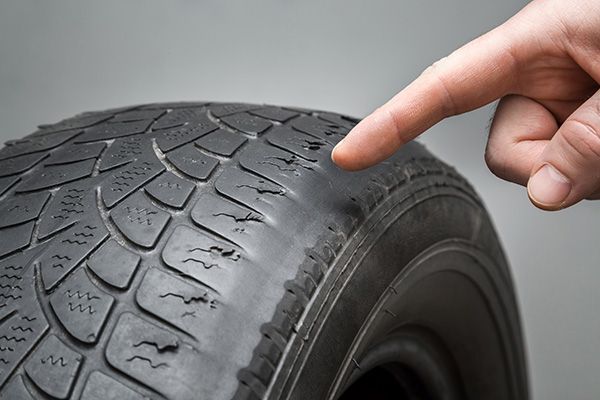 Finger pointing at worn, cracked tire with visible tread damage. | Auto Clinic Care