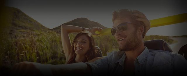 A couple enjoying a convertible ride through the countryside, smiling, with the woman's arm raised. | Auto Clinic Care