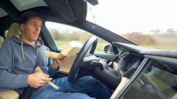 Man eating food while driving a car. He has a container of food, chopsticks, and is wearing a blue hoodie. | Auto Clinic Care