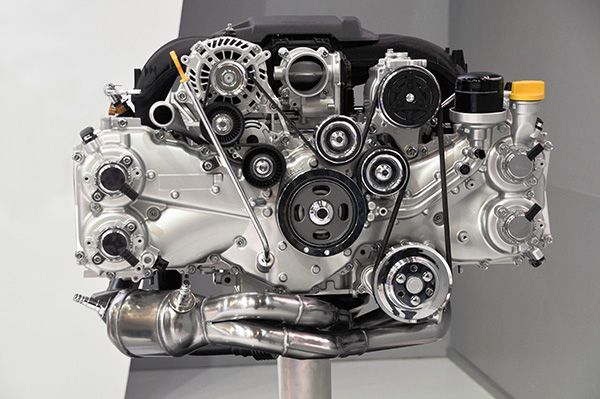 Silver car engine with various pulleys, belts, and exhaust manifold. | Auto Clinic Care