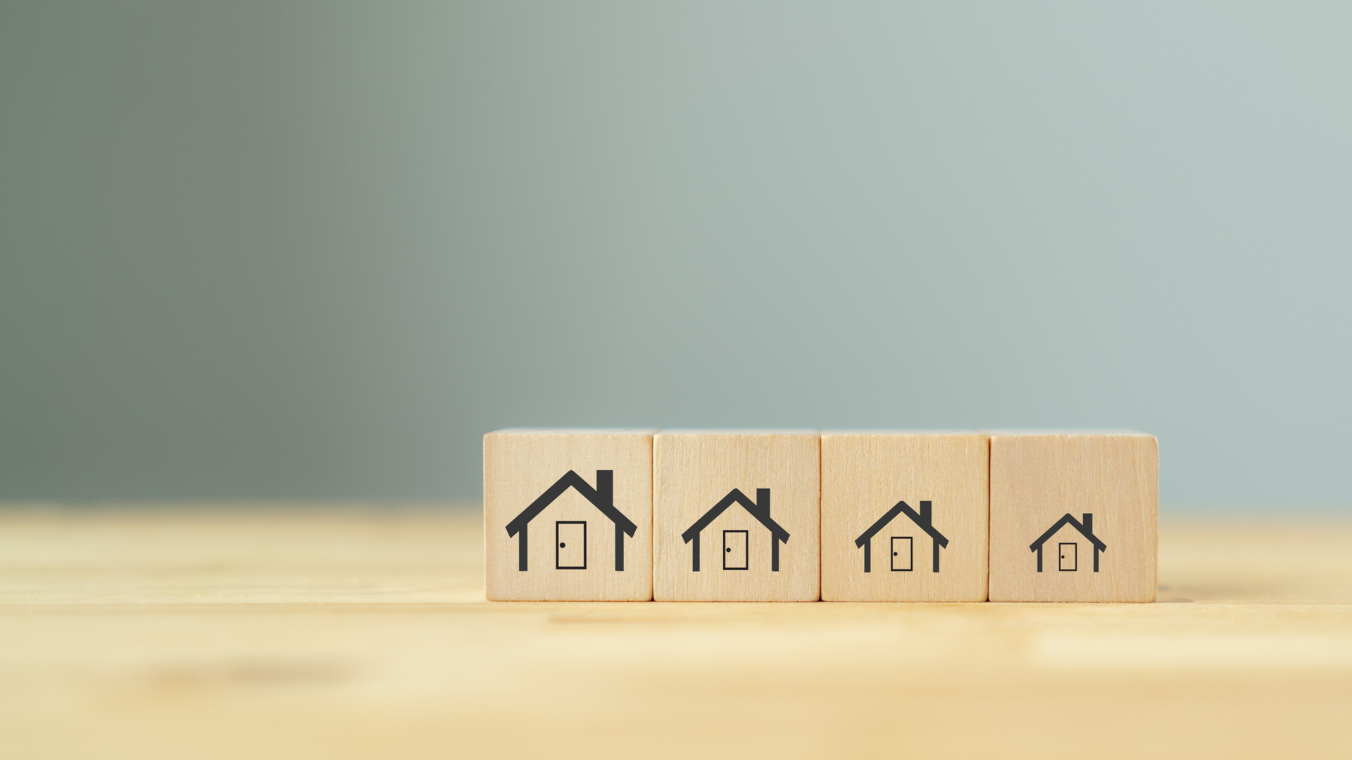 Wooden tiles with an image of a house stamped on them. The tiles are lined up in order with the houses getting smaller with each tile -representing downsizing.