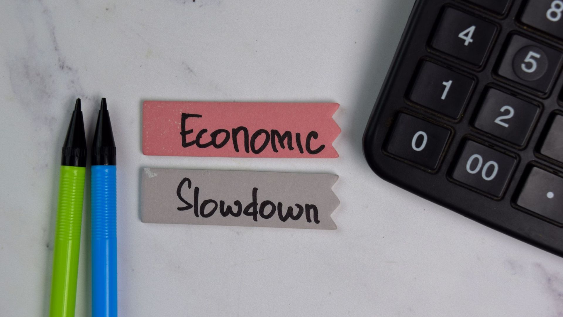 Photo of calculator, pencils and erasers with Economic Slowdown handwritten in Sharpie