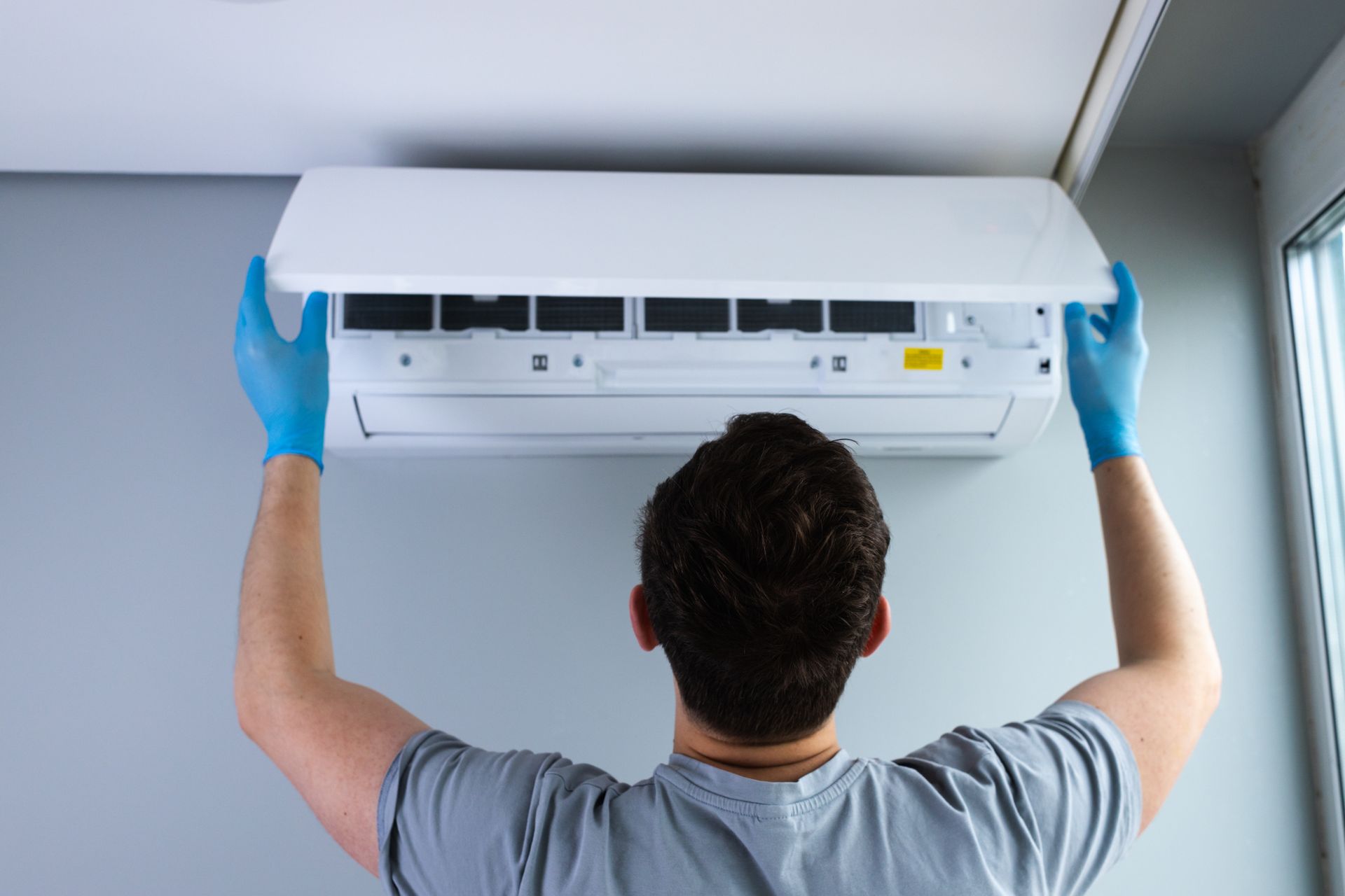 Technician in blue gloves installing a wall-mounted air conditioner indoors