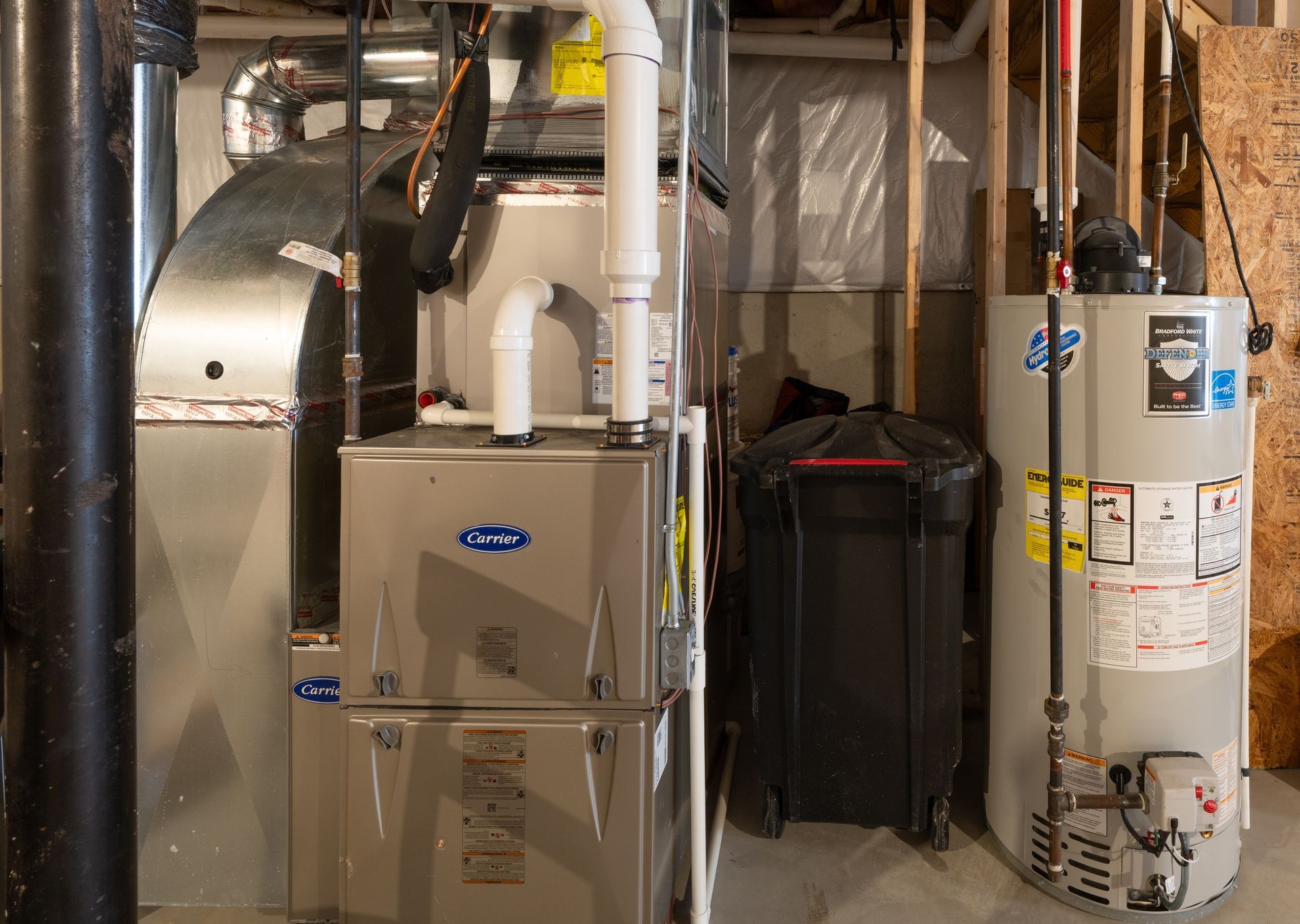 Basement utility room with furnace, water heater, ducts, and pipes