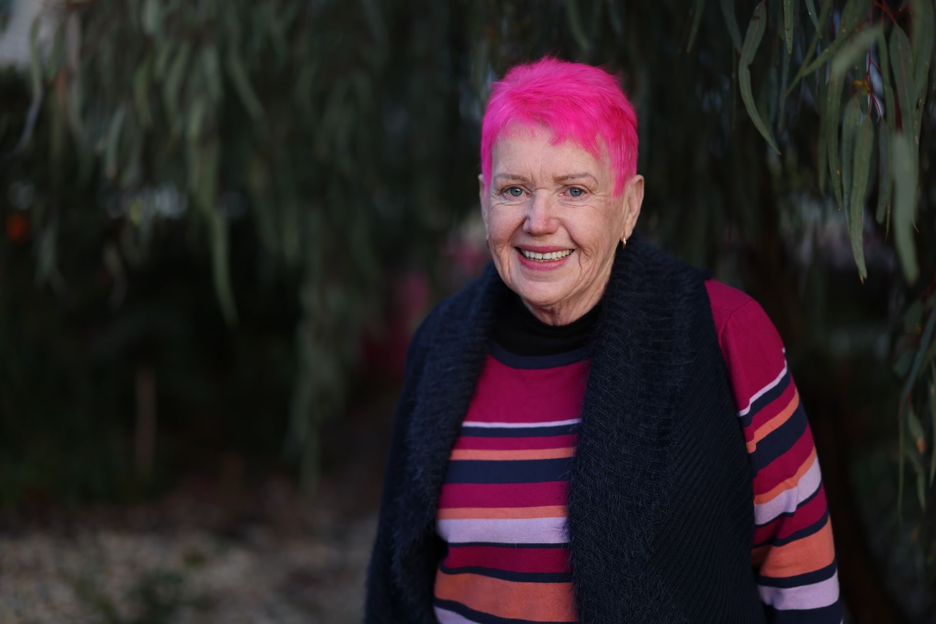 A Woman With Pink Hair Is Standing In Front Of A Tree And Smiling — Aged Care in Tamworth, NSW