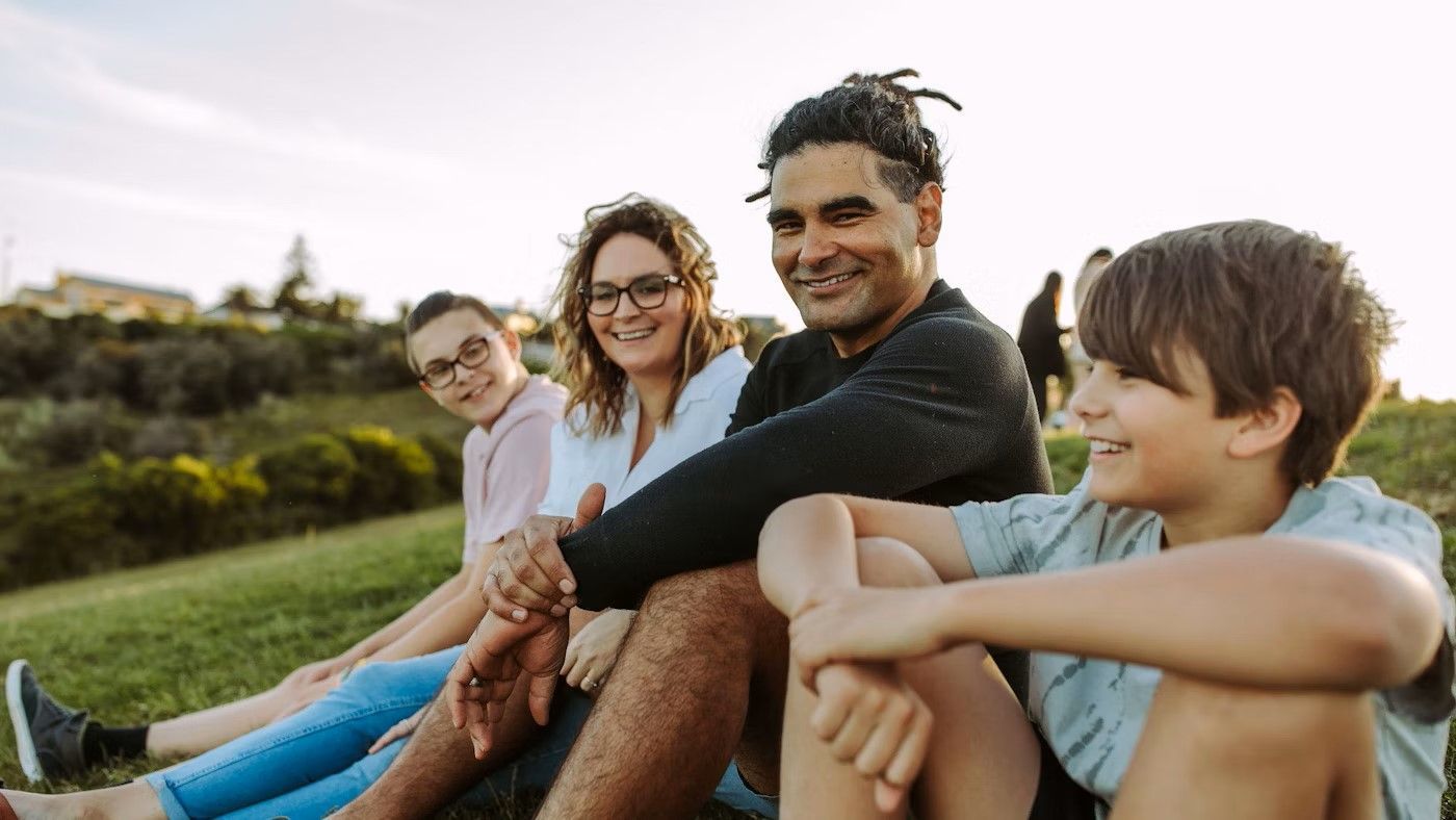 A Family Is Sitting On The Grass In A Park — Aged Care in Tamworth, NSW