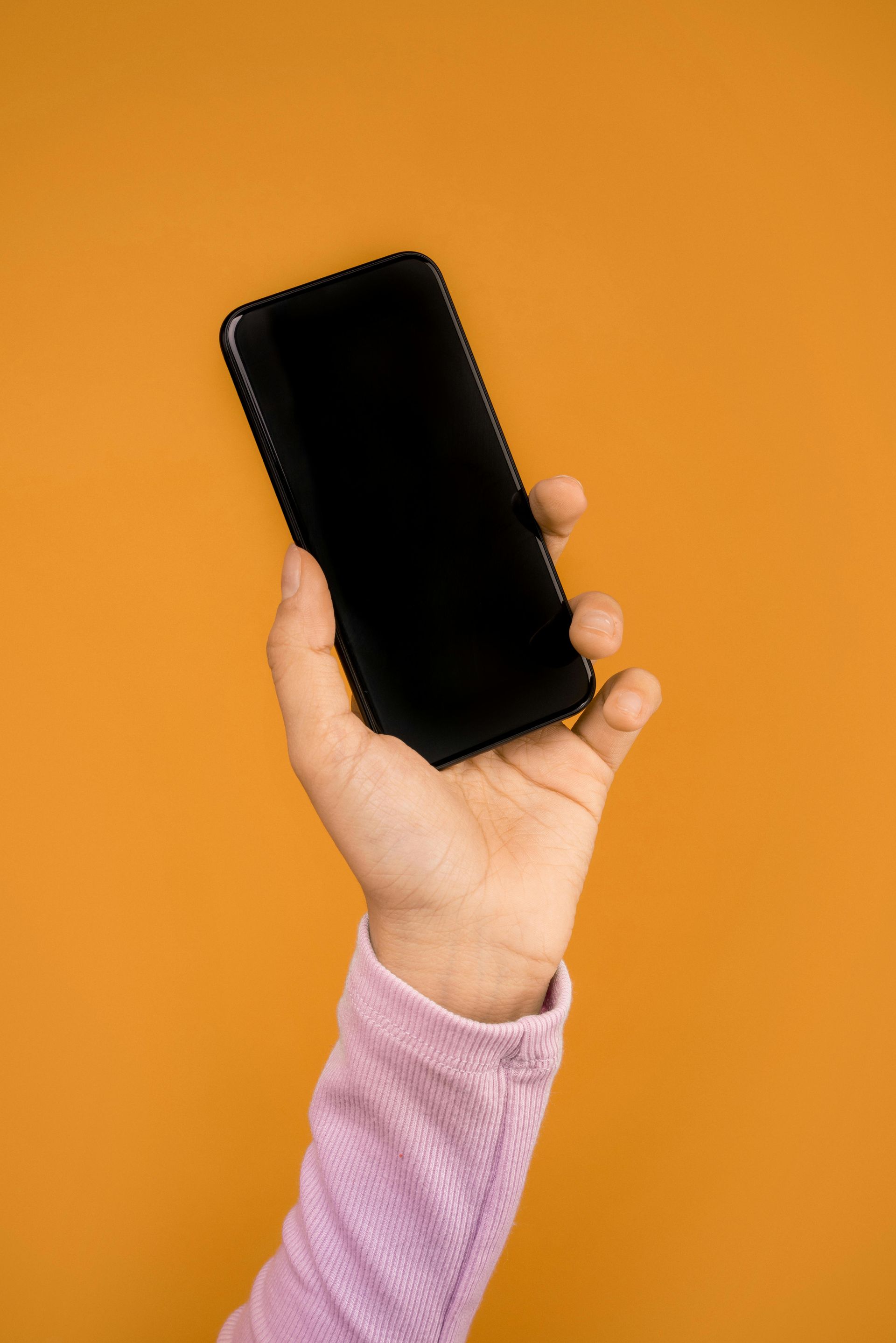 A Person Is Holding A Cell Phone In Their Hand Against An Orange Background — Aged Care in Tamworth, NSW