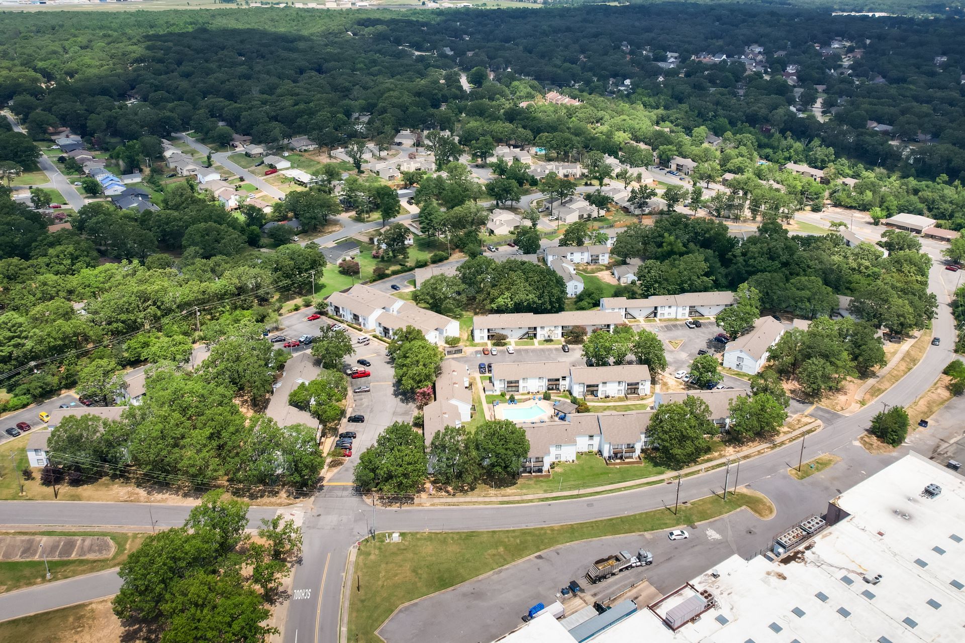 Aerial view of residential neighborhood with white buildings, trees, and roads on a sunny day.