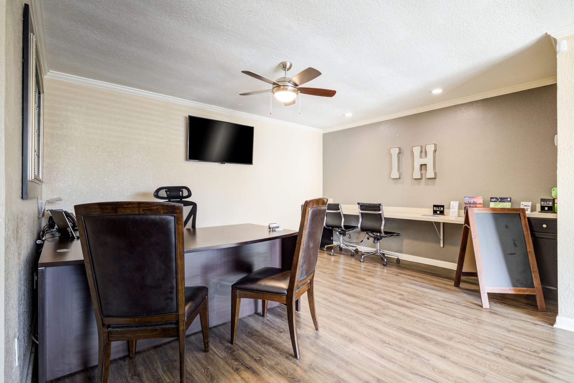 An office with a desk, chairs, a TV, and a blackboard. Wooden floors and a ceiling fan.