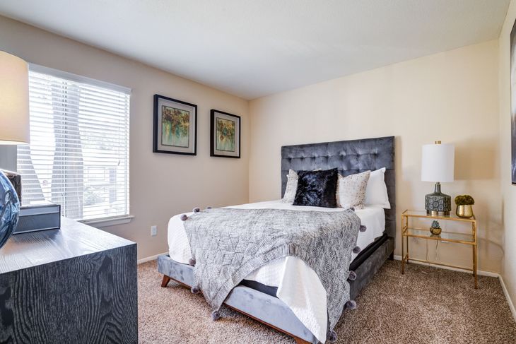 Bedroom with a gray bed, two framed pictures, a window, and a gold side table.