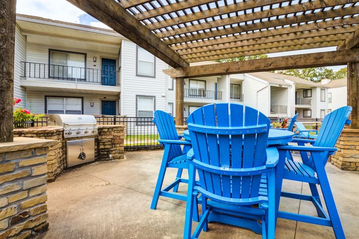 Outdoor patio with blue chairs, a grill, and apartment buildings in the background.
