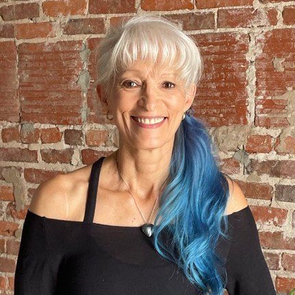 cecile  with white hair and blue hair is smiling in front of a brick wall .
