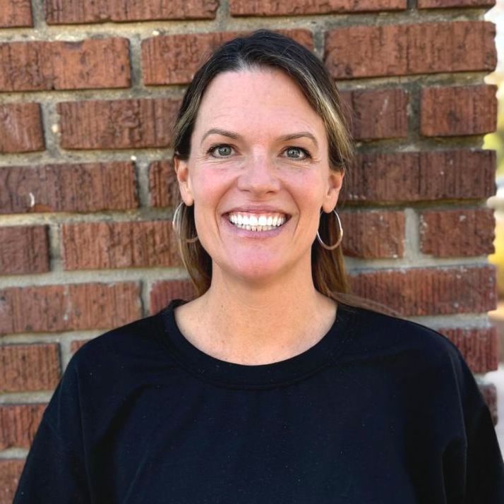 Stephaine in a black shirt is smiling in front of a brick wall.