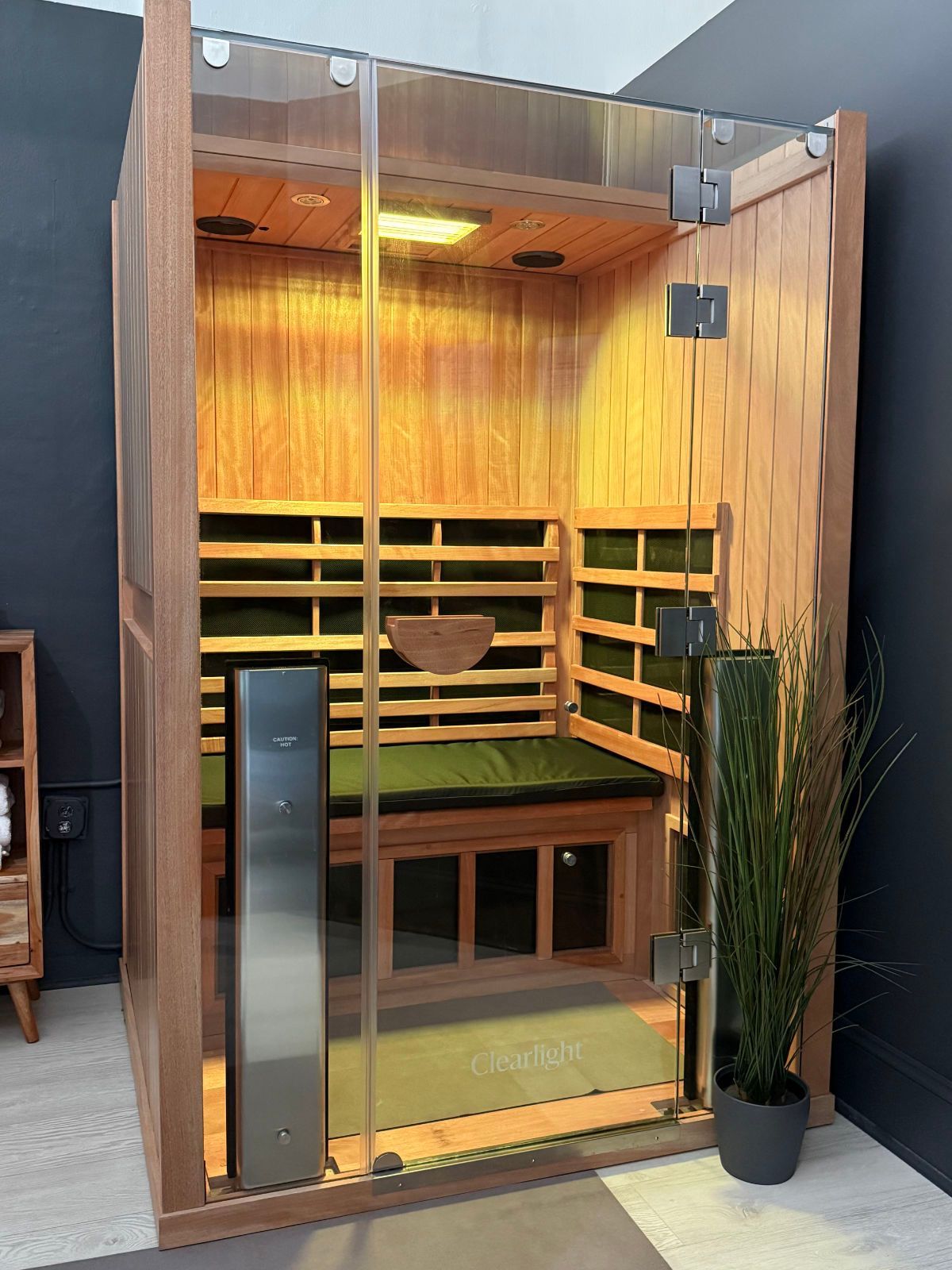 Wooden sauna with glass door, bench, and infrared heaters, illuminated interior.