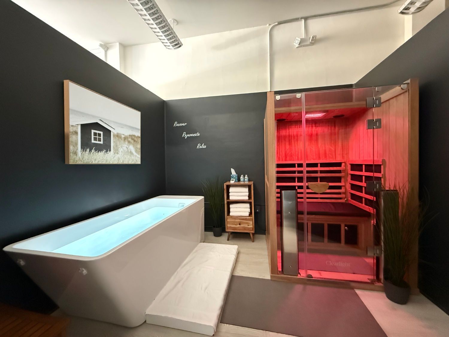 A spa room with a soaking tub, sauna, and towels on a wooden cabinet, all in a modern setting.