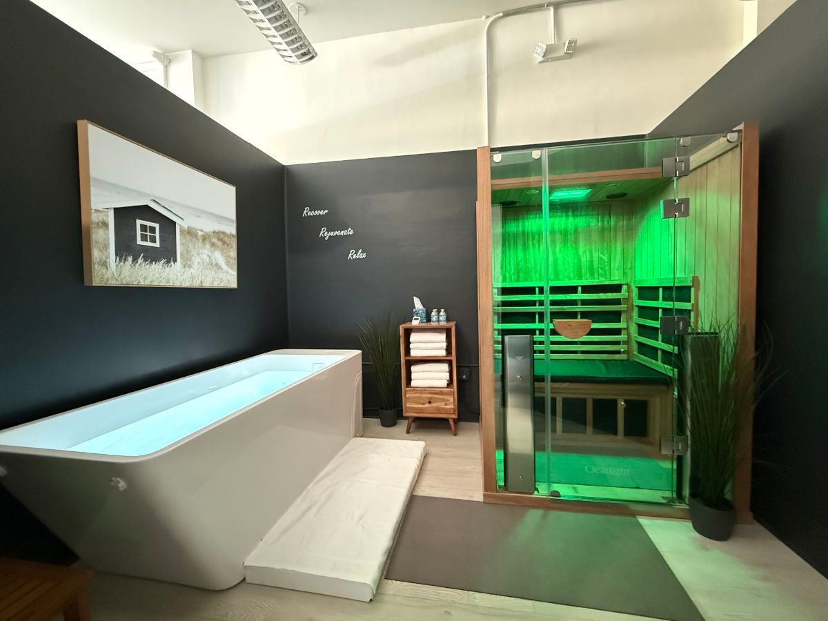 A spa room with a bathtub, sauna, and decor against dark walls. Green lighting inside sauna.