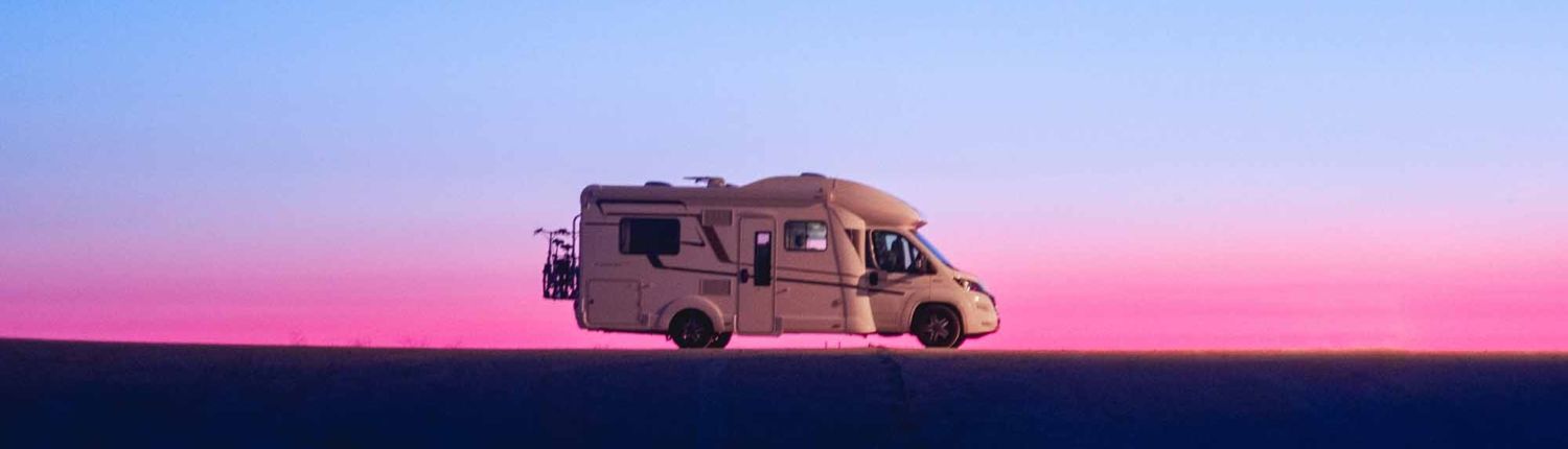 A rv is driving down a road at sunset.