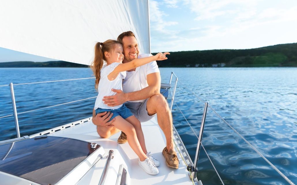 A man and a little girl are sitting on a sailboat in the water.