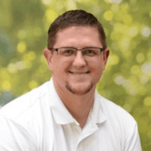 A man wearing glasses and a white shirt is smiling for the camera.