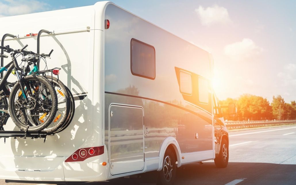 A rv with two bikes attached to the back is parked on the side of the road.