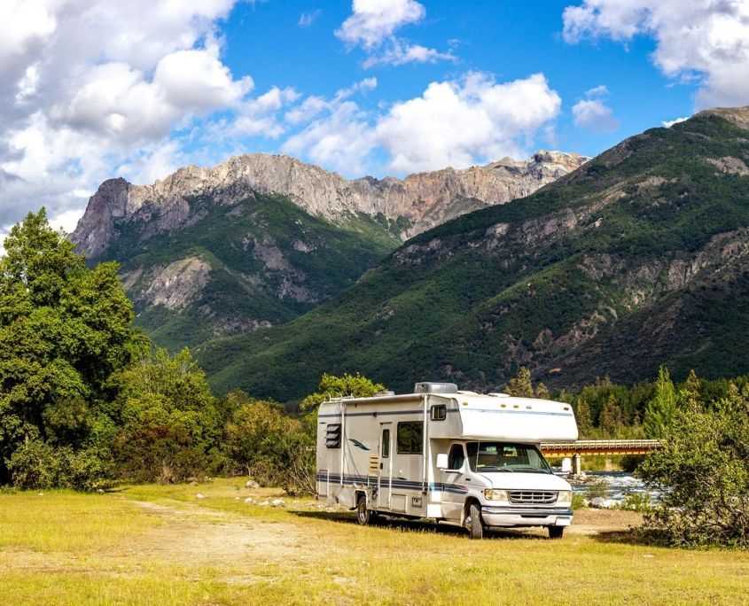 A rv is parked in a grassy field with mountains in the background.