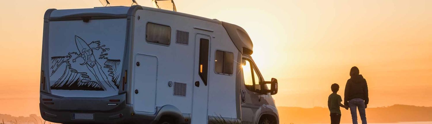 mother and son watching the sunset with their motor home at the edge of the sea