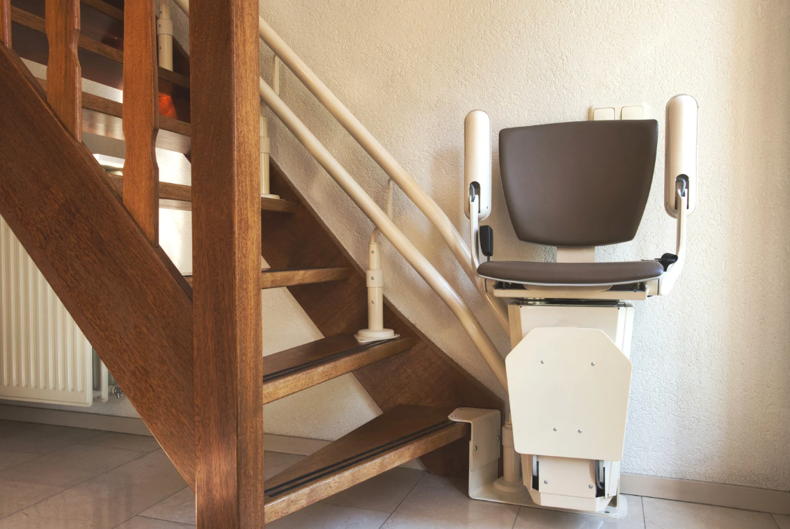 Stair lift installed along a wooden staircase, with a seat and railings attached to the wall.
