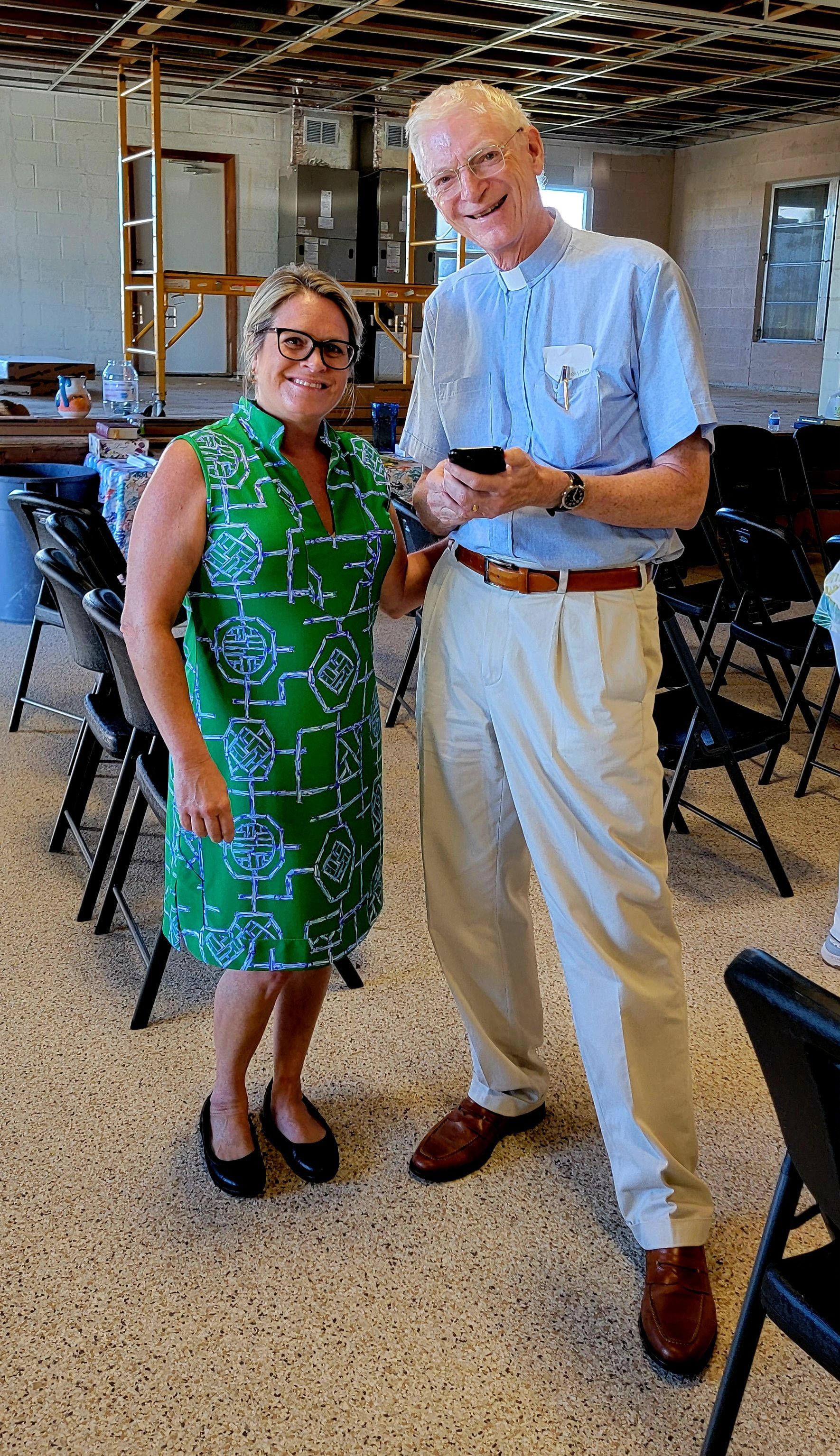 Woman in green dress and tall man in light pants smile, posing indoors.