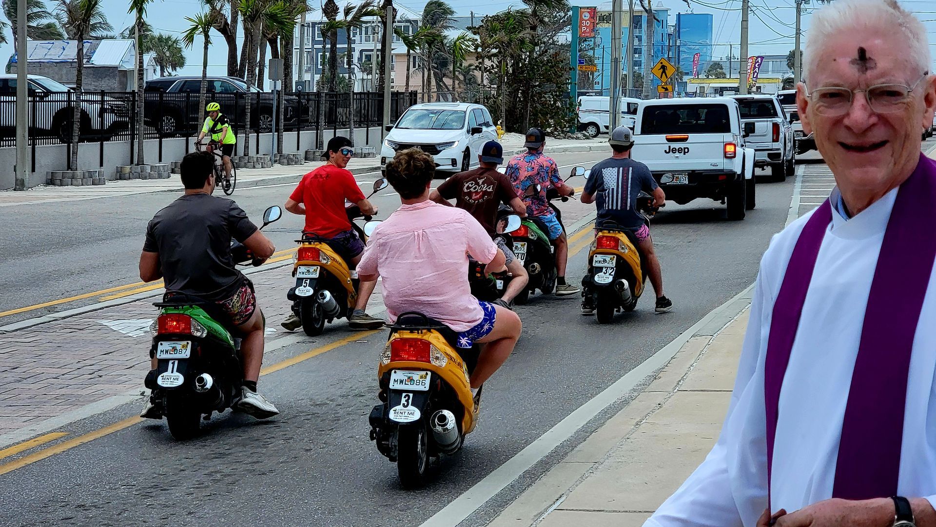 Priest with ashes on forehead smiles at scooter riders on a sunny street.