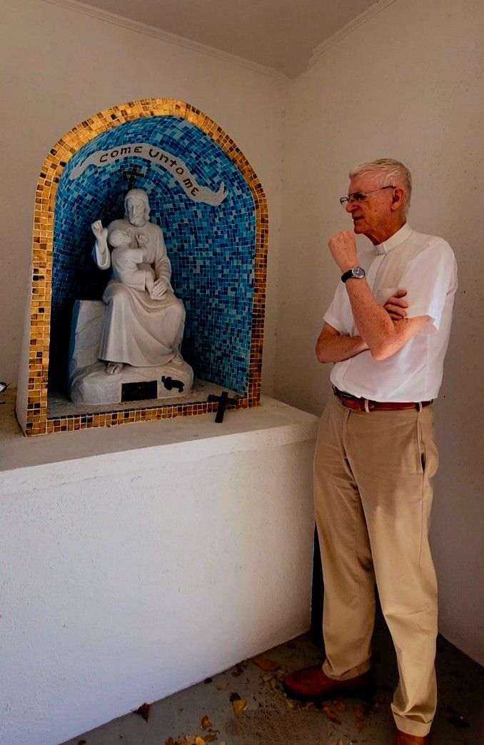 Man in khaki pants and white shirt looks at a statue in a mosaic-decorated niche.