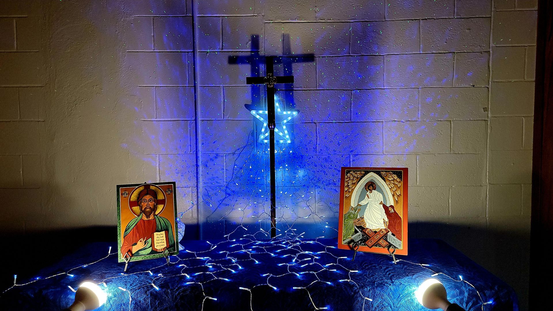 Altar with cross, blue star, icons, and twinkling lights on a brick wall.