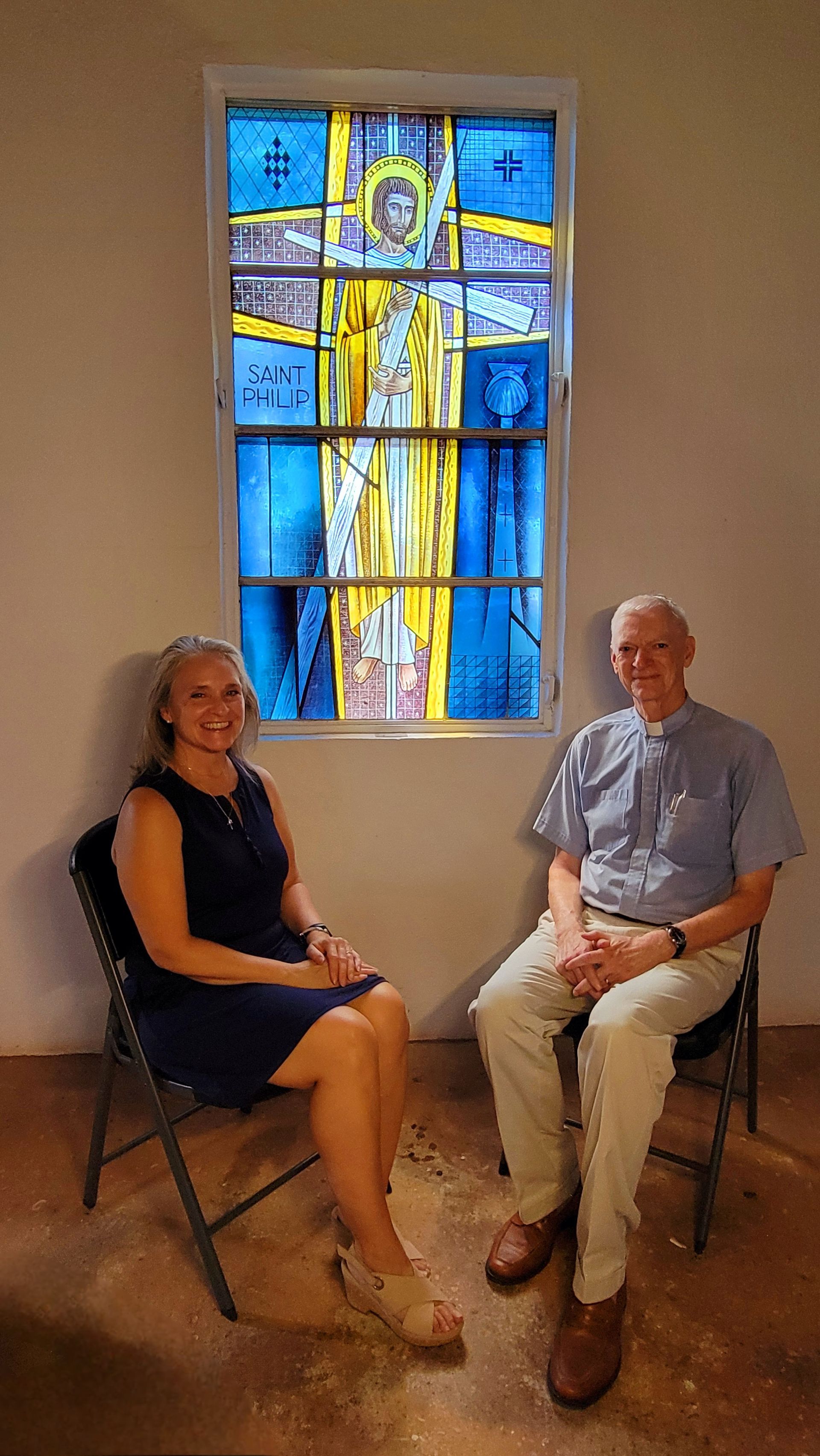 Woman and man sitting in front of stained glass window with blue, yellow, and white colors.