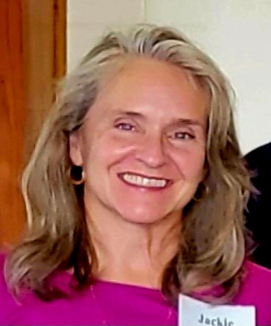 Smiling woman with graying hair in a pink top, wearing earrings.