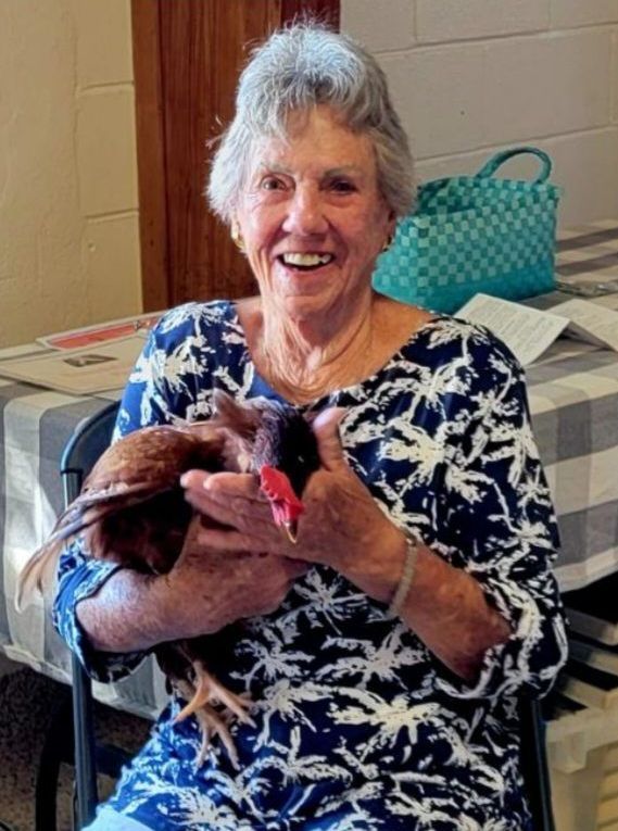 Smiling elderly woman in blue print top holds a chicken.