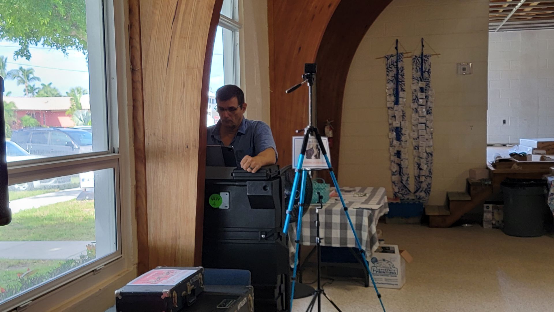 Man at a computer near a window, working in a bright room with equipment and decor.