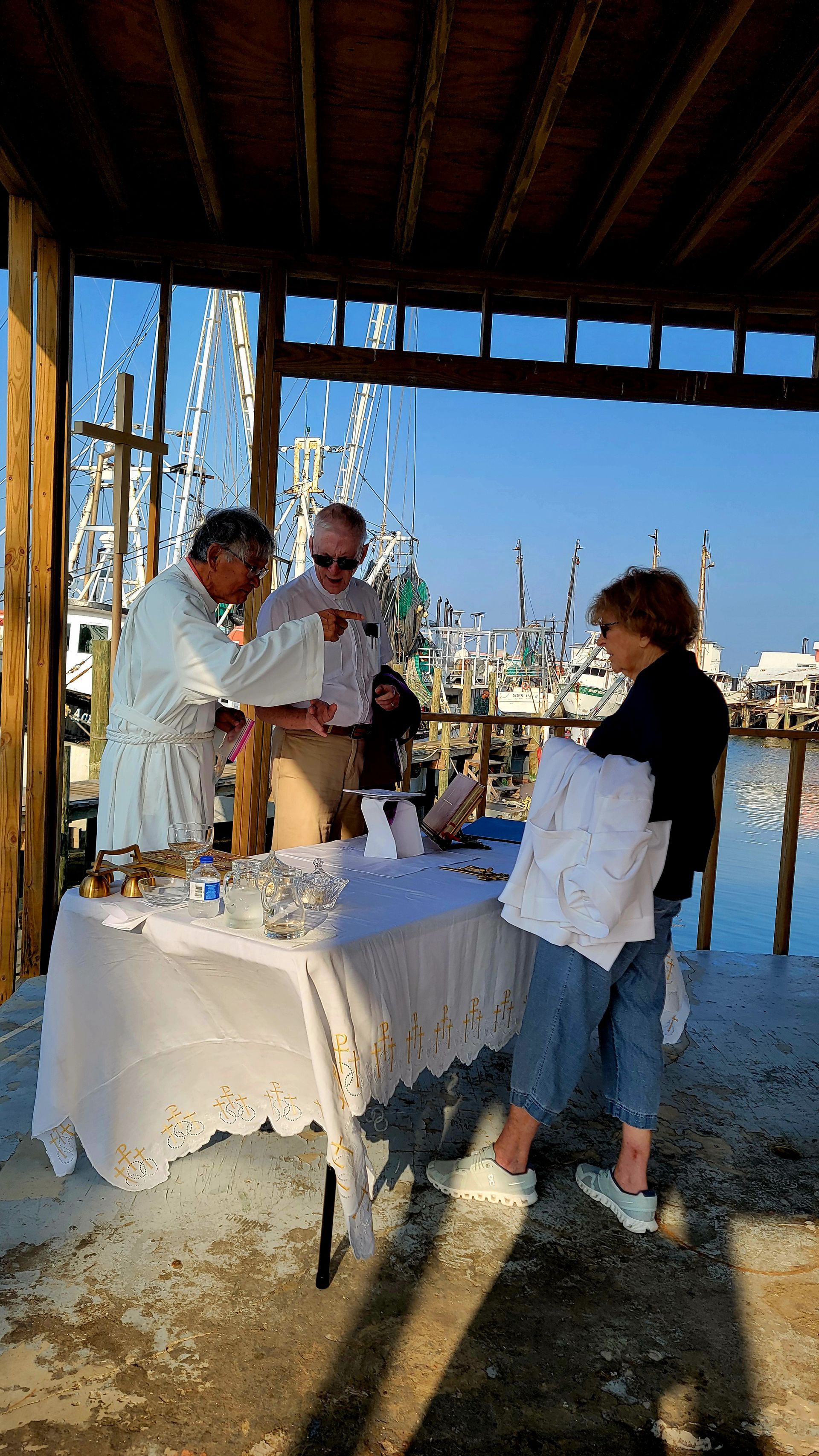 People at an outdoor event, selecting items from a table by a pier.